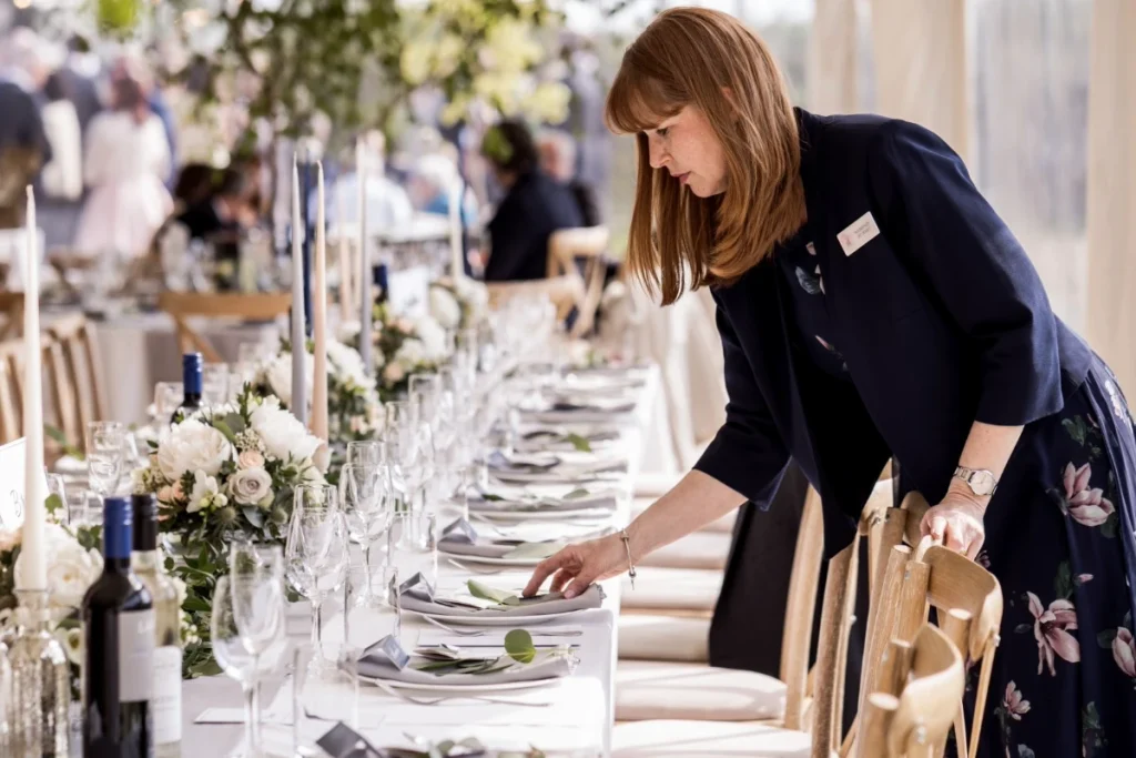 Seorang wedding organizer menata meja makan dan perlengkapan untuk persiapan acara pernikahan.