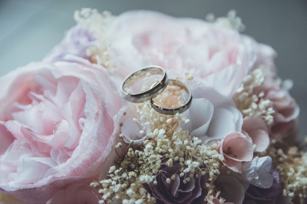 Dua cincin pernikahan diletakkan di atas rangkaian bunga merah muda dan putih untuk menggambarkan intimate wedding sederhana.
