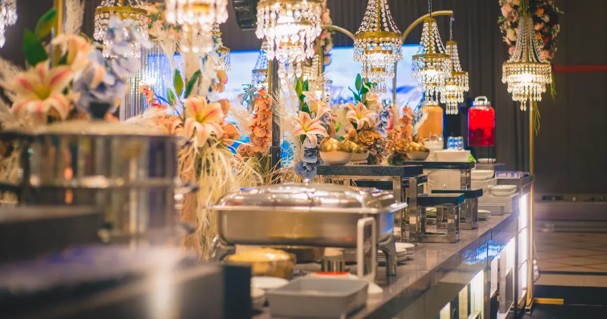 Buffet catering pernikahan dengan berbagai hidangan, peralatan saji, bunga, dan dekorasi meja untuk tamu.