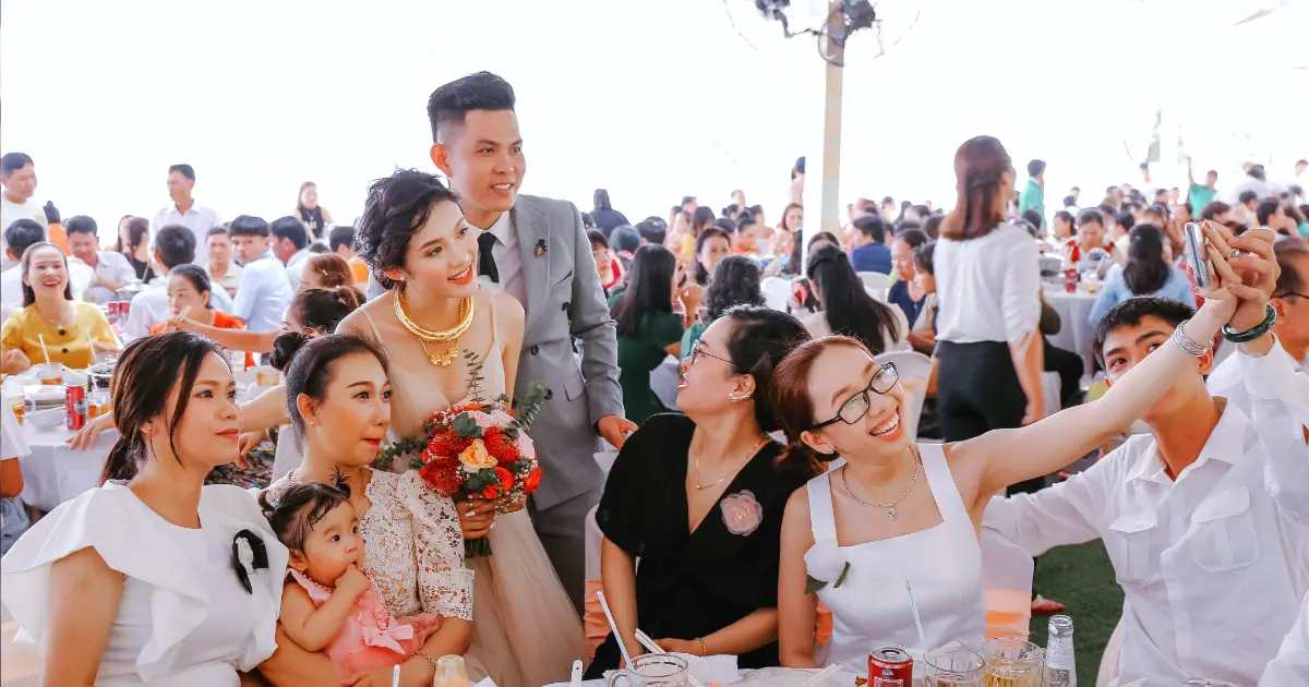 Pengantin berfoto bersama tamu saat menikmati hidangan dalam acara pernikahan dengan suasana pesta yang ramai.