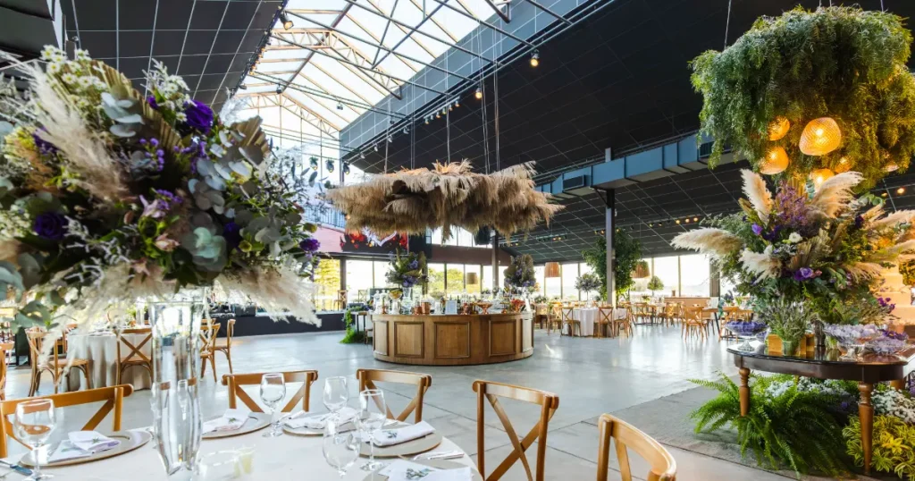 Venue resepsi pernikahan dengan meja makan, dekorasi bunga, area catering, dan suasana ruangan yang luas.